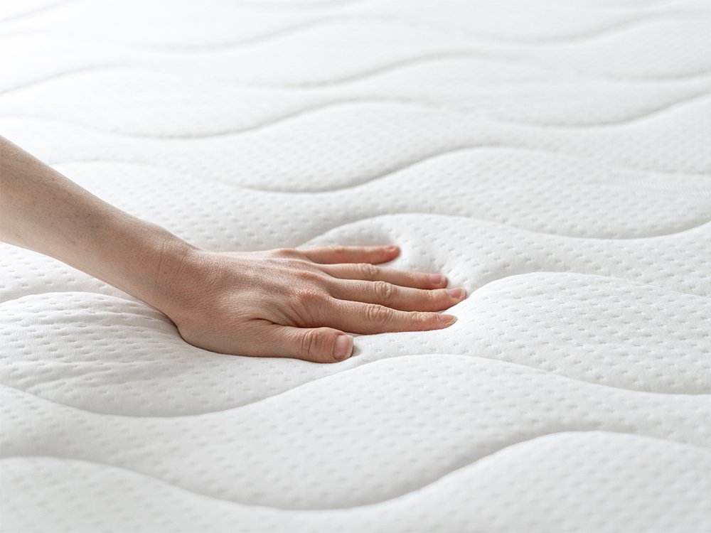 Hand pressing into a plush white quilted mattress